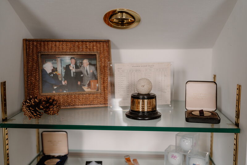 A shelf of golfing memorabilia including a framed photograph, medals, a trophy and a scorecard beneath a brass wall light