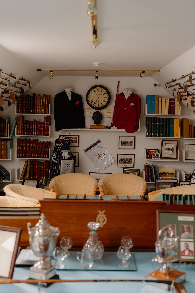 Vintage club blazers hung either side of a wall clock, golf bags and shelves of books filling a memorabilia room