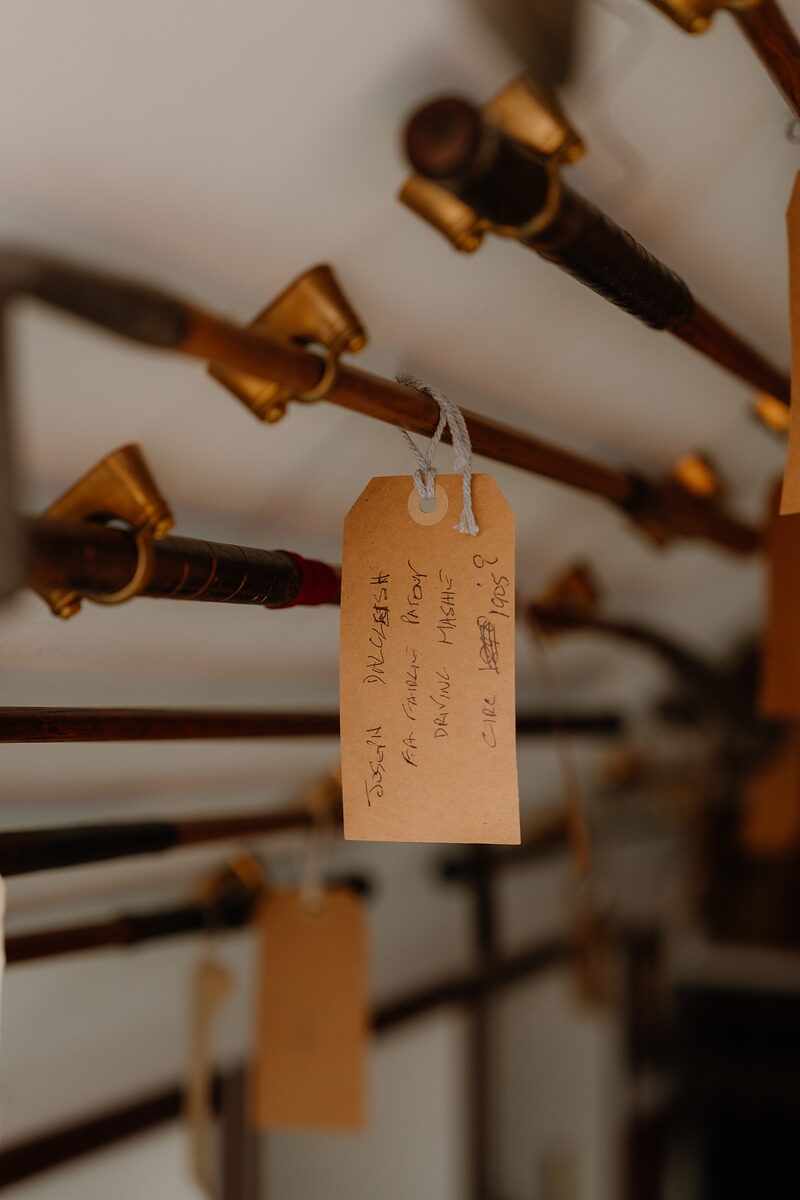 Golf clubs with brass ferrules hanging in a row, a handwritten luggage tag attached to one