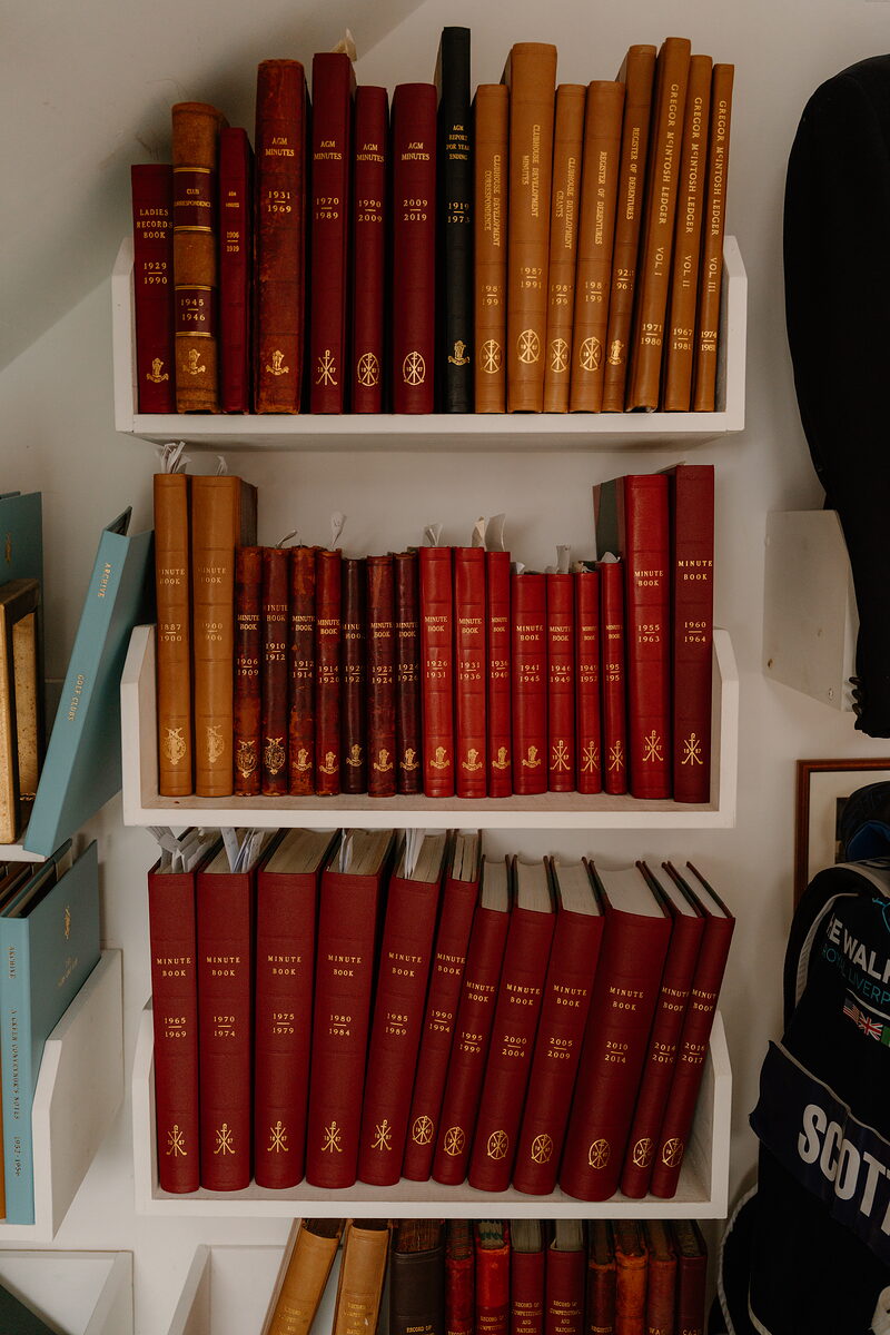 Rows of leather-bound minute books and club records lined up on shelves in a clubhouse archive