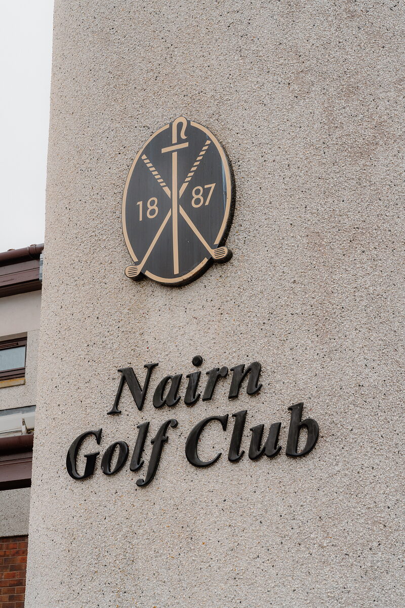 A carved crest above the lettering Nairn Golf Club mounted on a stone pillar