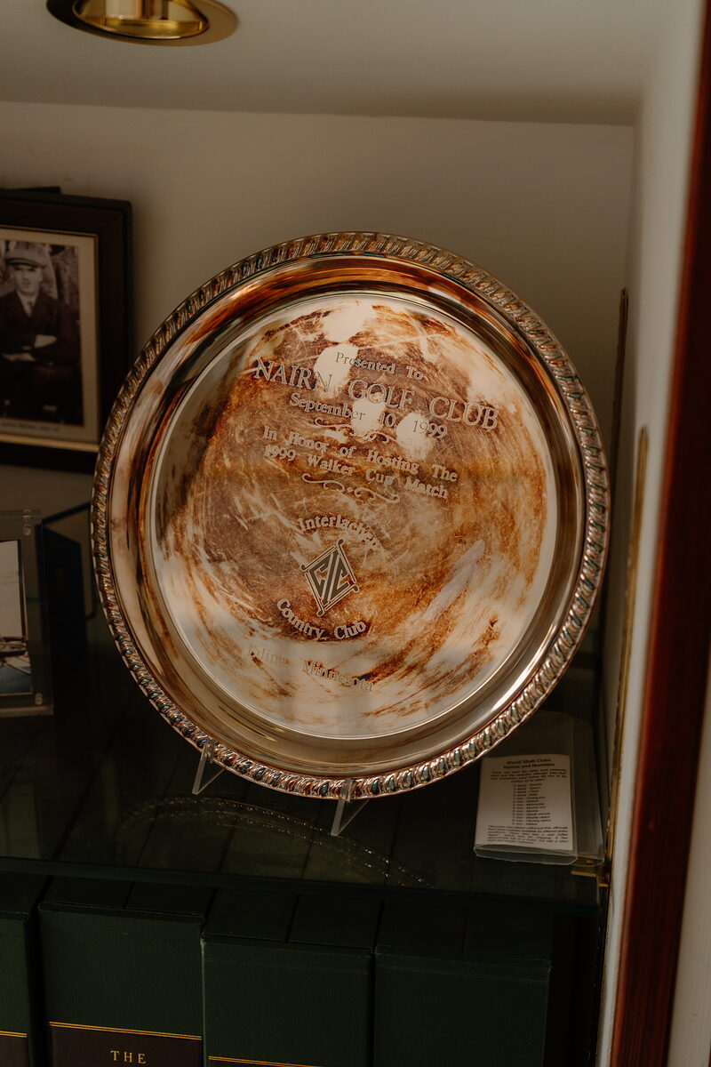 An engraved silver salver presented to Nairn Golf Club, displayed on a stand beside framed photographs