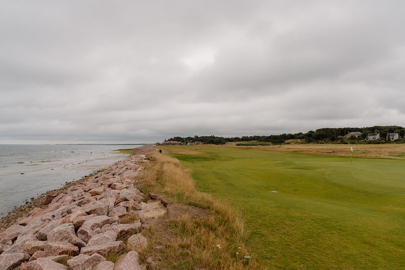 A fairway bordered by pink rock armour, trees and rooftops lining the horizon