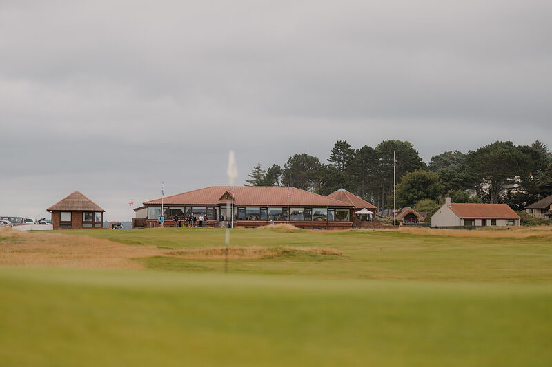 A firework bursting above a clubhouse, small figures gathered on the lawn below