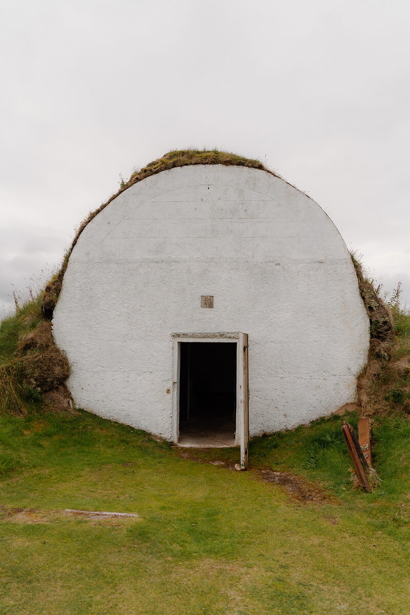 A rounded whitewashed shelter with an open timber door set into a grassy bank