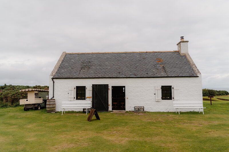 A whitewashed cottage with a slated roof and shuttered windows, a bench and water butt set outside