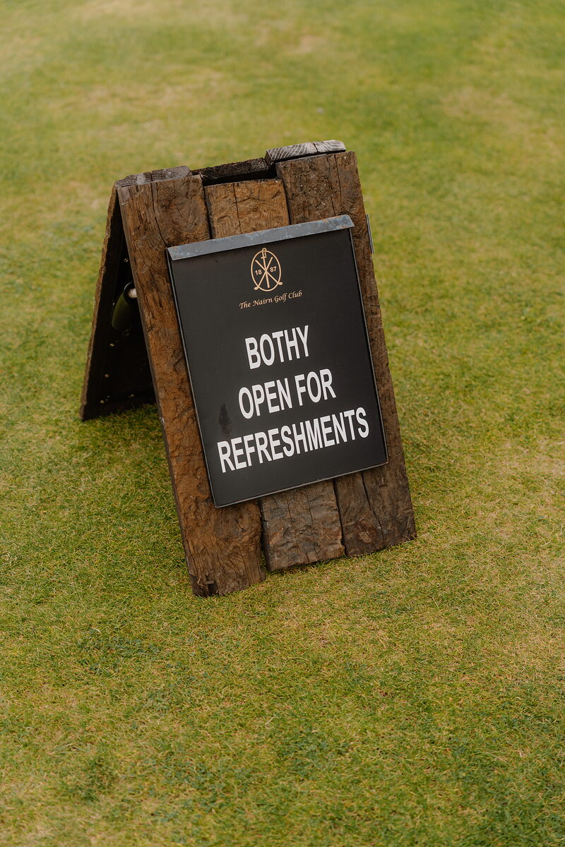 A wooden sandwich board reading Bothy Open For Refreshments standing on a fairway
