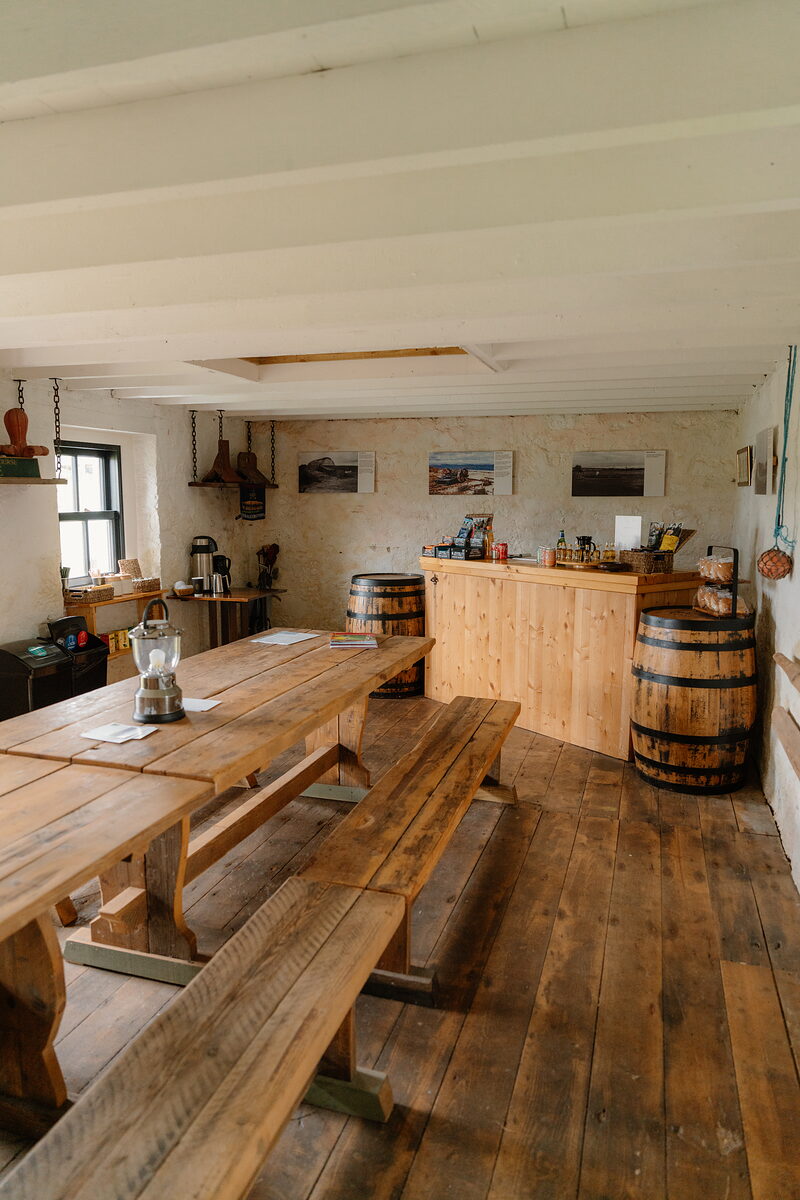 A rustic dining room with wooden tables and benches, barrels and framed prints set against the far wall