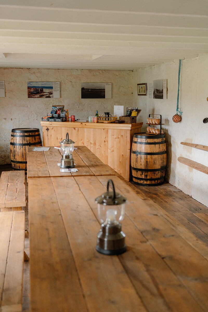 A rustic dining room with wooden tables and lanterns, barrels and framed photographs set against the walls