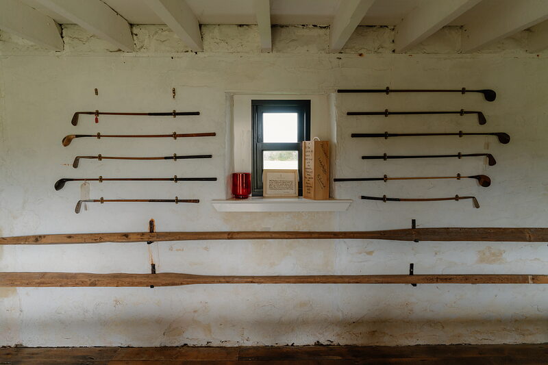 Rows of antique golf clubs mounted on a whitewashed wall either side of a small window
