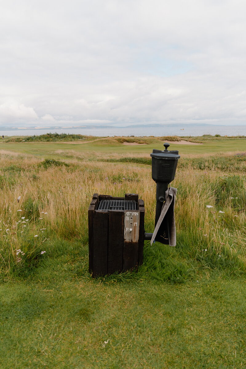 A litter bin and ball-washing stand on the fairway at Nairn, sea and dunes in the background