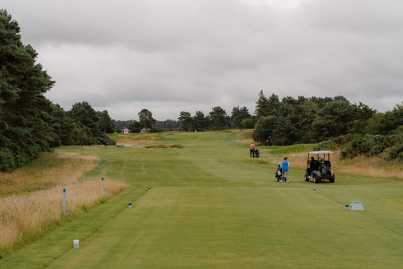 Golfers with a buggy setting off down the fairway at Nairn under an overcast sky