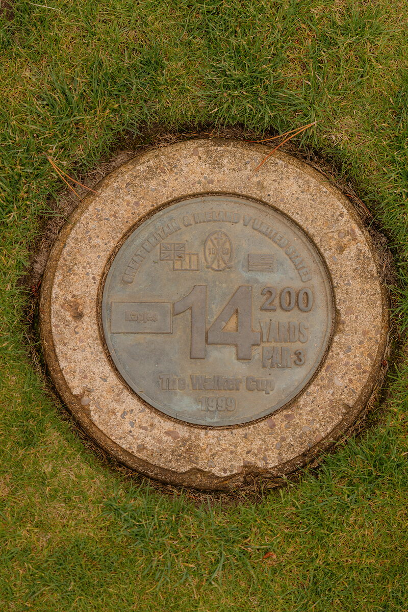 A bronze yardage marker set into the turf, engraved with the hole number and Walker Cup 1999