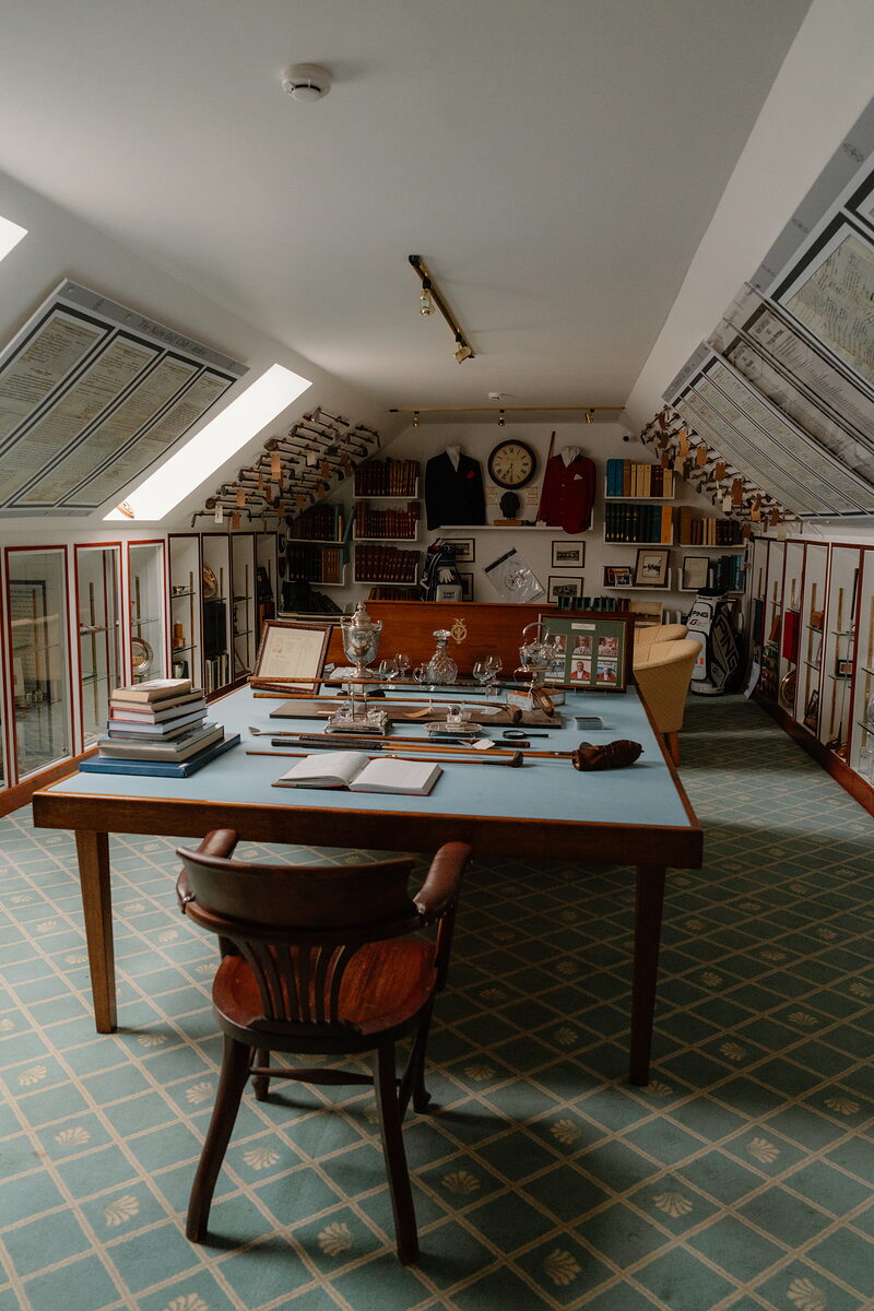 A heritage room displaying old golf clubs, blazers and trophies in glass cabinets around a central table
