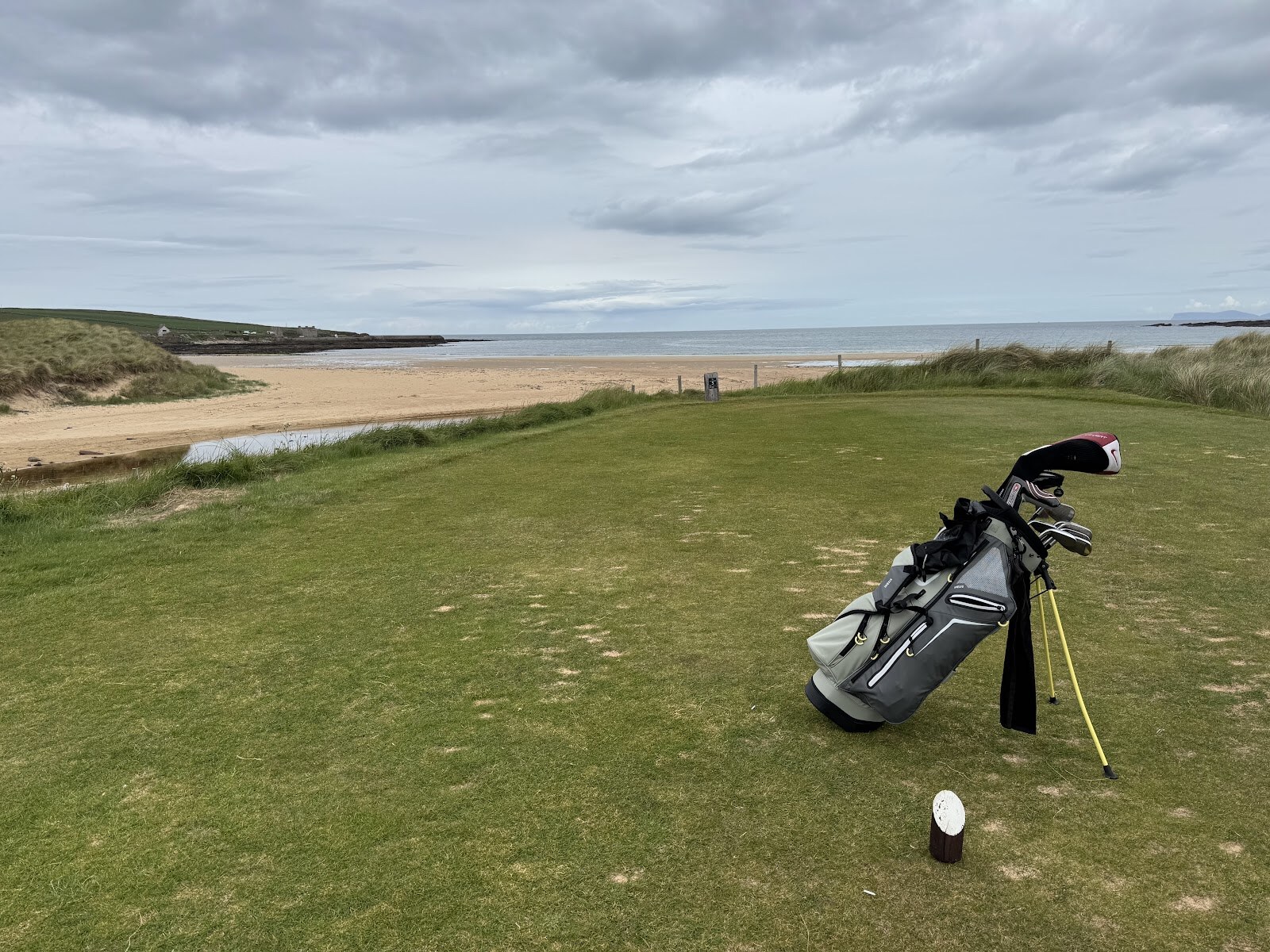 A golf bag on a tee above the beach of Sandside Bay, with a burn running out across the sand.