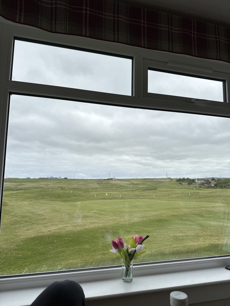 The view from a clubhouse window over Reay’s greens and fairways, with tulips in a glass on the sill.