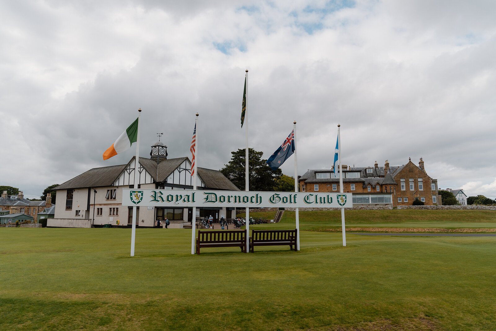 The Royal Dornoch Golf Club sign flanked by flagpoles before its black-and-white timbered clubhouse