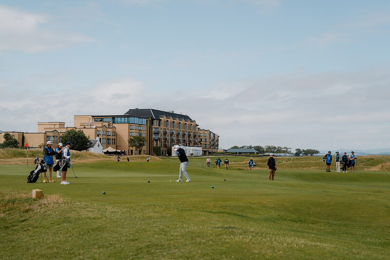 Golfers putting on a green at St Andrews Links, the Old Course Hotel rising behind them.