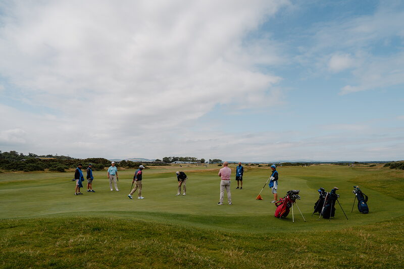 Golfers putting on a green at St Andrews Links, their bags set together nearby.