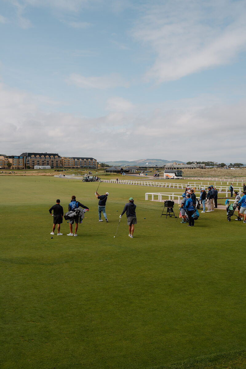 Golfers finishing a round at St Andrews Links, Hamilton Hall's turreted building rising behind.
