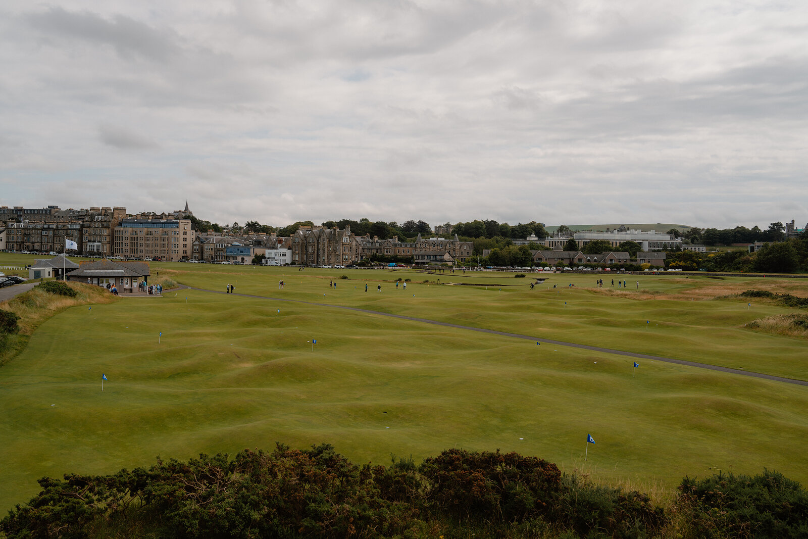 A wide view of the Old Course at St Andrews Links, golfers scattered across the fairway with the town beyond.