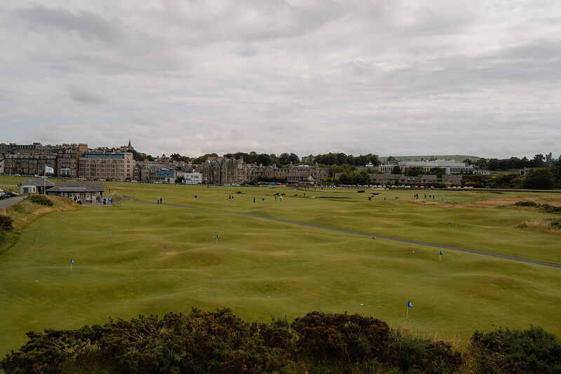 A wide view of the Old Course at St Andrews Links, golfers scattered across the fairway with the town beyond.