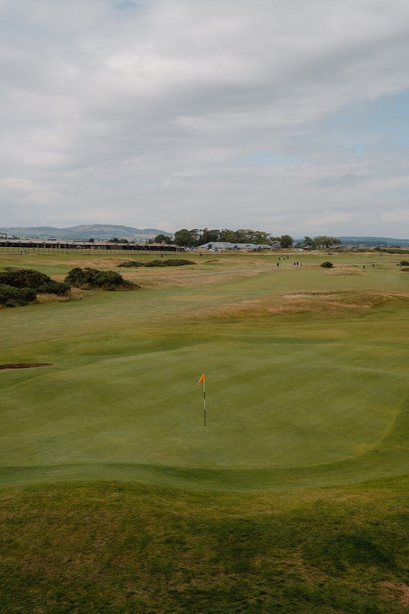 A golf green at St Andrews Links, the flag marking the hole with the town's buildings beyond.