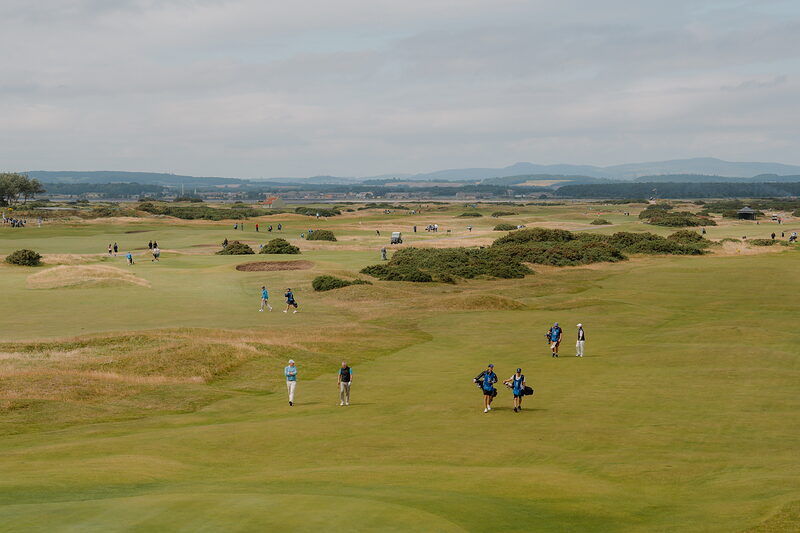Golfers walking across the fairway at St Andrews Links, bunkers dotting the rough beyond.