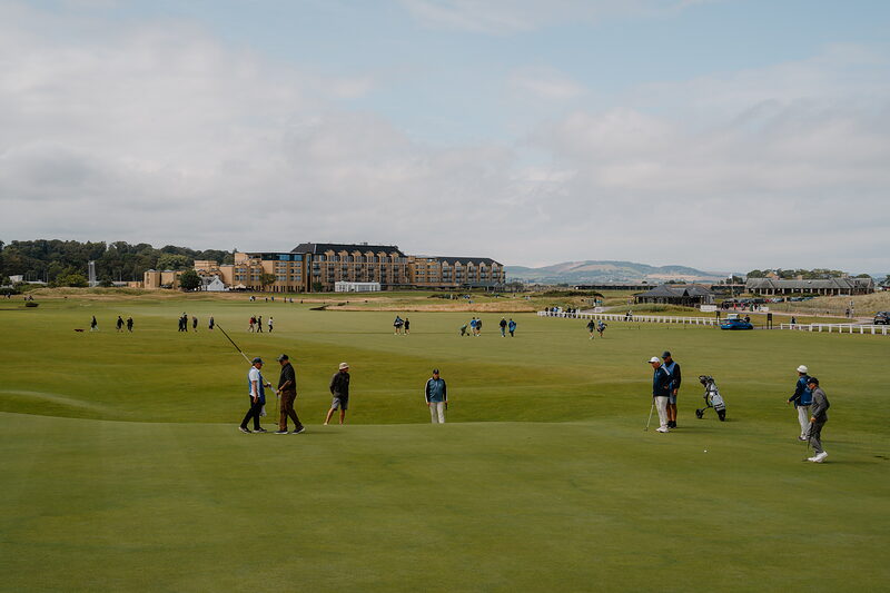 Golfers crossing the fairway at St Andrews Links, a grand hotel building rising behind.