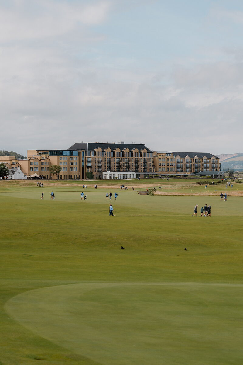 Golfers cross a green with the Hamilton Grand building rising behind them.