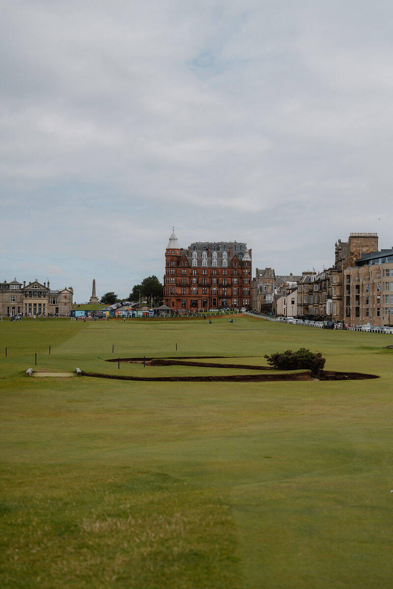A red-brick hotel and an obelisk rise beyond the Old Course's fairway and bunkers.