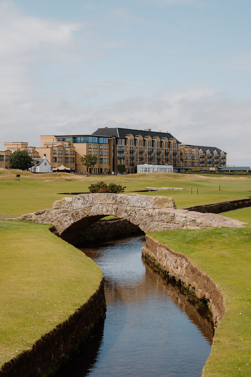 The Swilcan Bridge arches over its burn, a grand hotel rising behind on the Old Course.