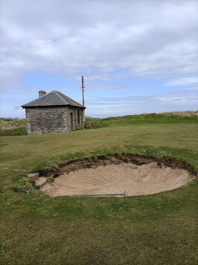 The stone cable house and its telegraph pole behind a round bunker on Wick’s links.