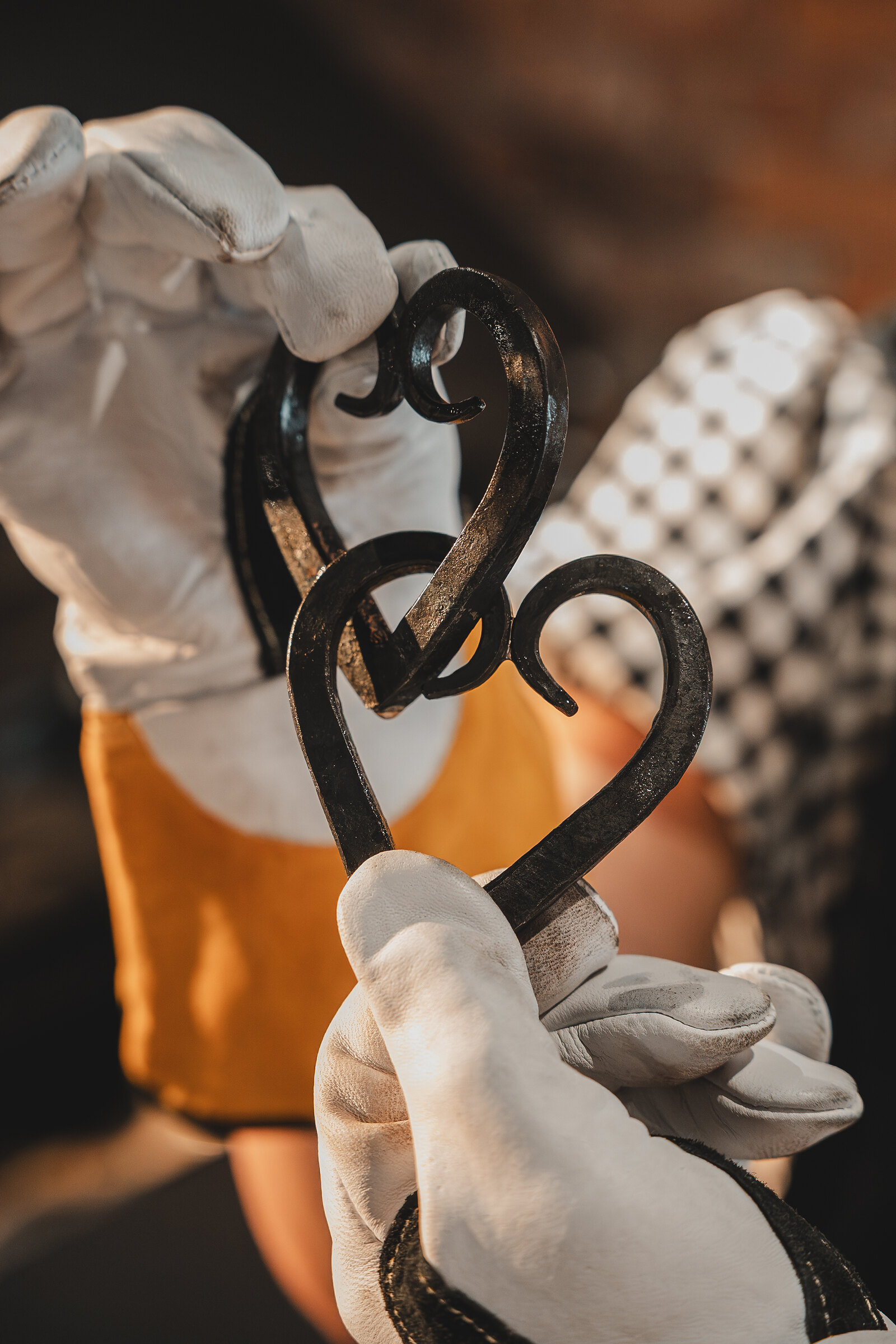Gloved hands hold up two iron hearts, forged and twisted together.