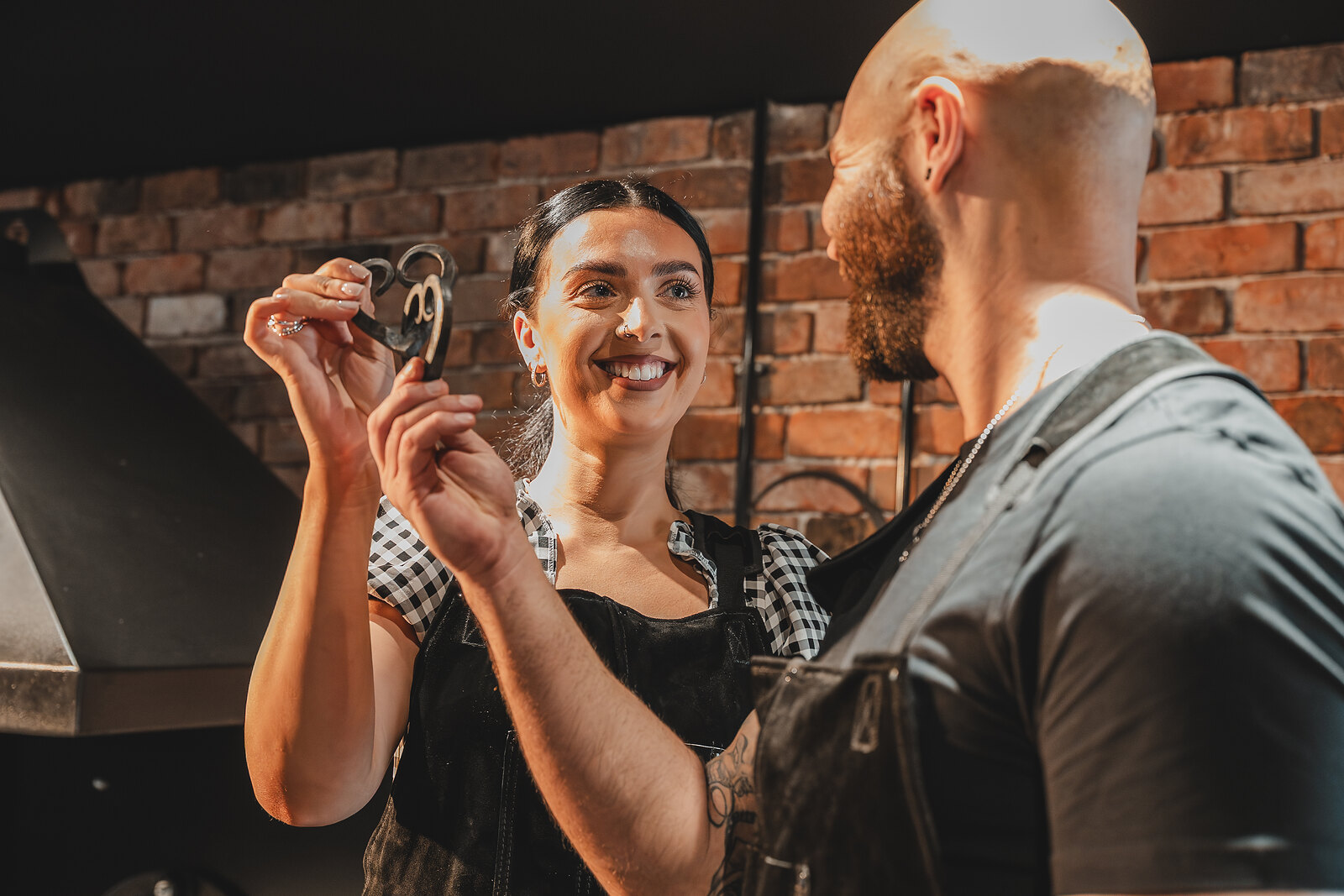 A woman beams as she holds up the pair of entwined iron hearts she and her partner have forged.