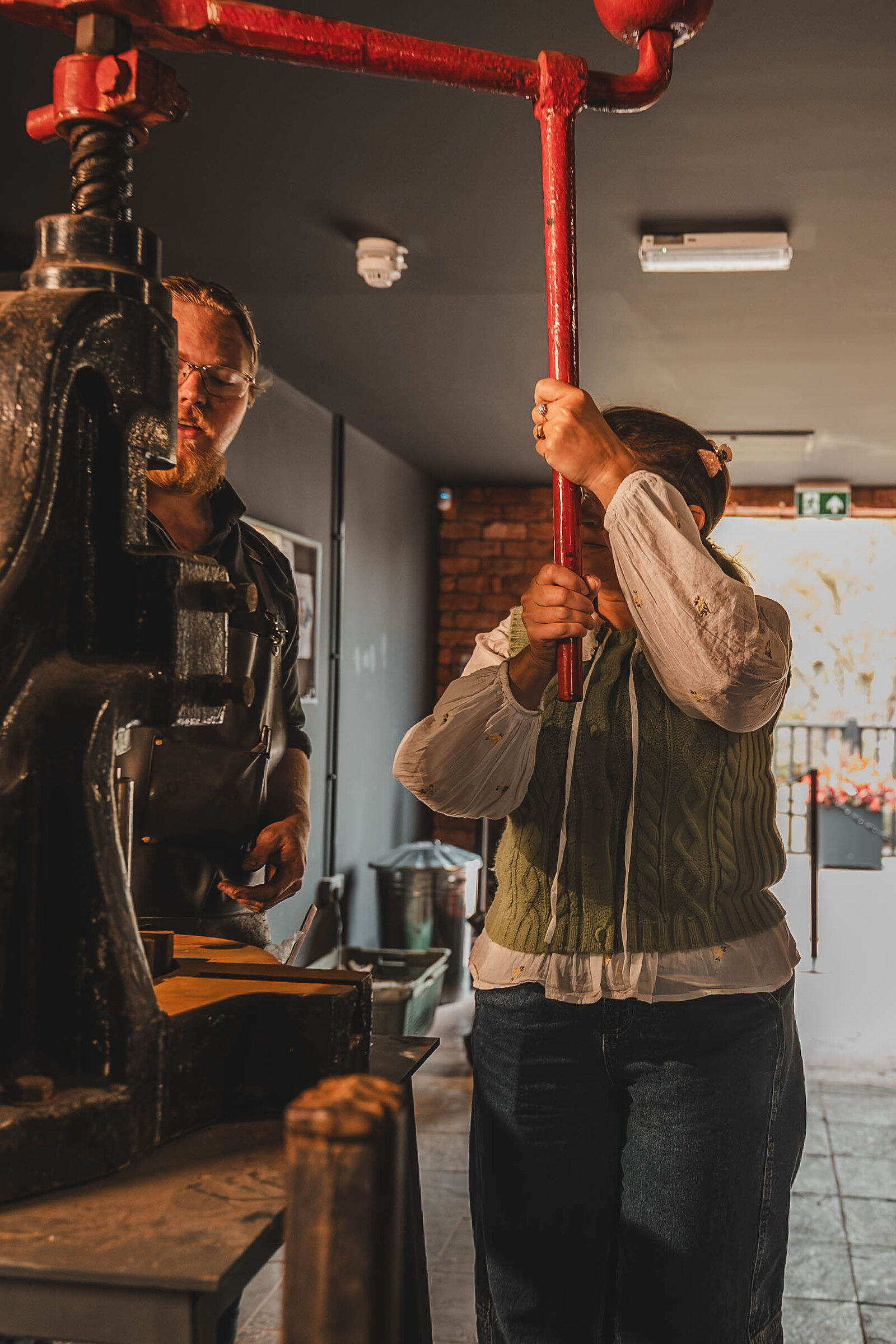 A visitor hauls down on the red lever of the coin press at the Gretna Green Forge.