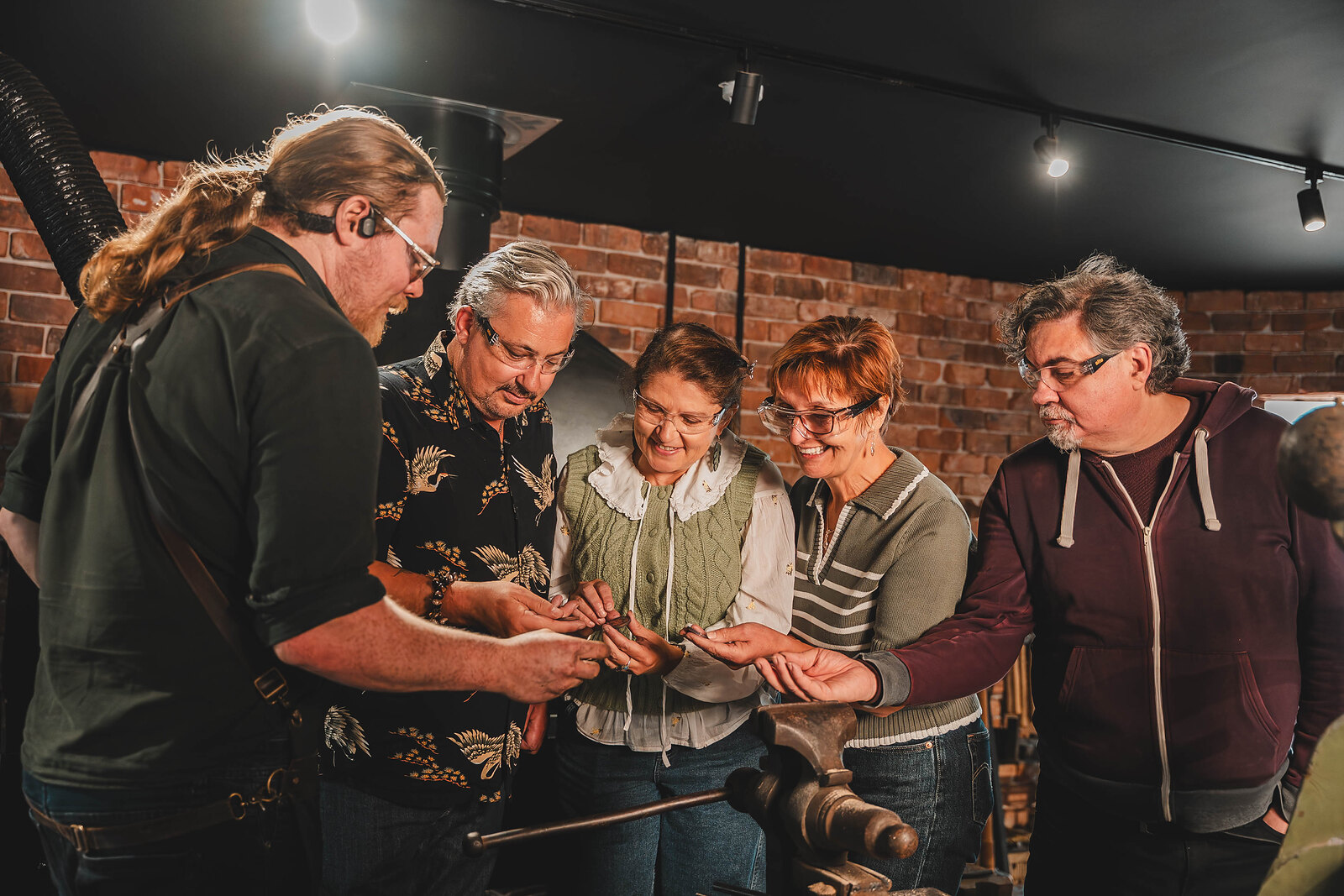 A group gathers round the blacksmith at the Forge, holding out the coins they have just made.
