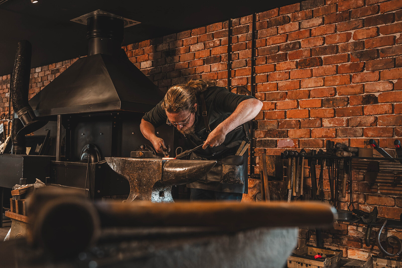 The blacksmith at work at the anvil in the new Gretna Green Forge, its hooded hearth behind him.