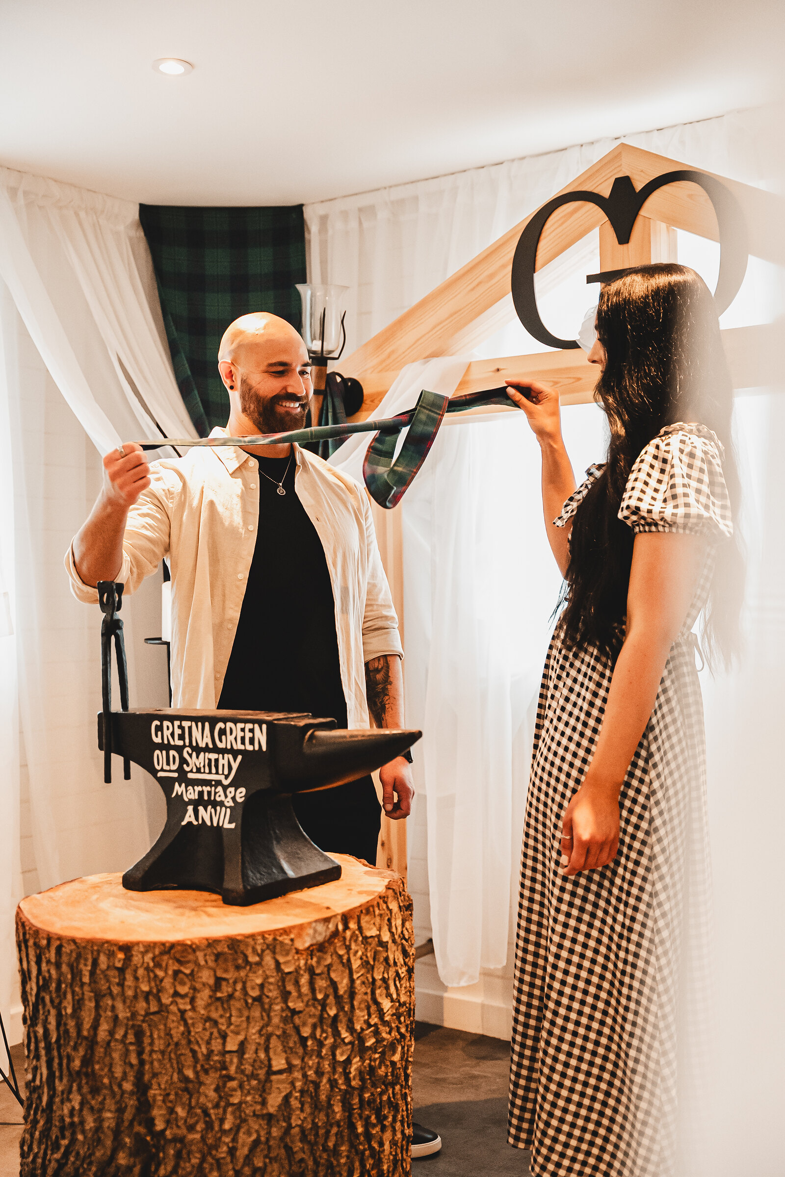 A couple face each other across the Gretna Green Marriage Anvil as a tartan ribbon is wrapped round their hands.