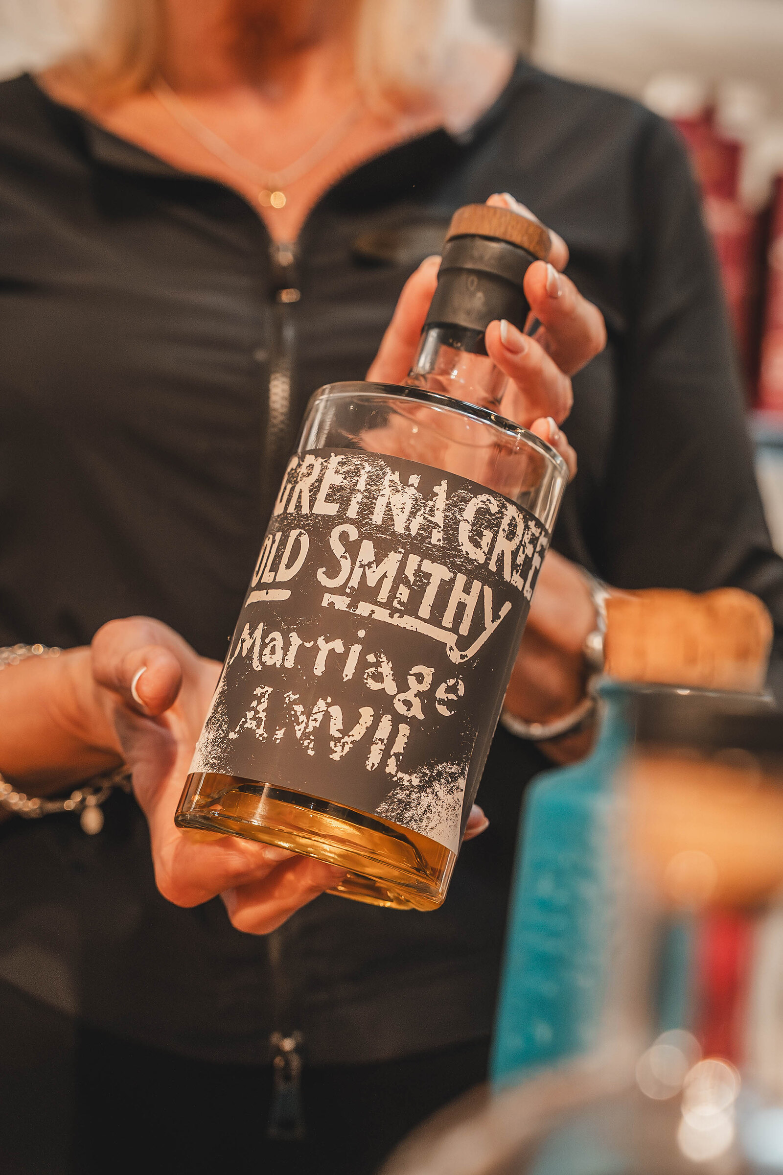 A host holds up a bottle of Gretna Green Old Smithy Marriage Anvil spirit.