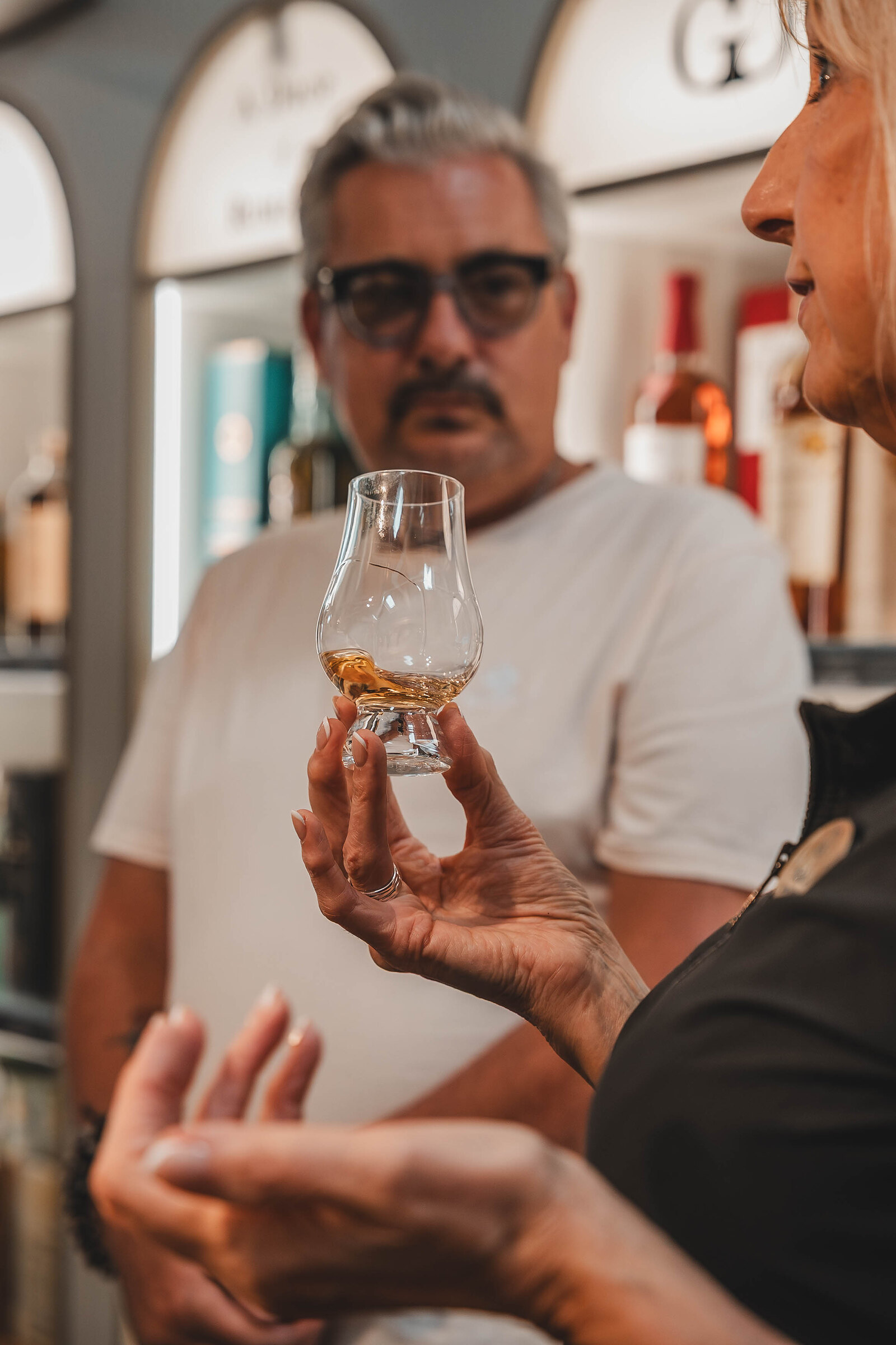 A man in glasses studies the whisky in his tasting glass.