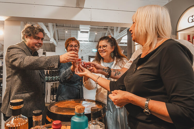 Friends raise their tasting glasses round a barrel table at the First Sip of Scotland.