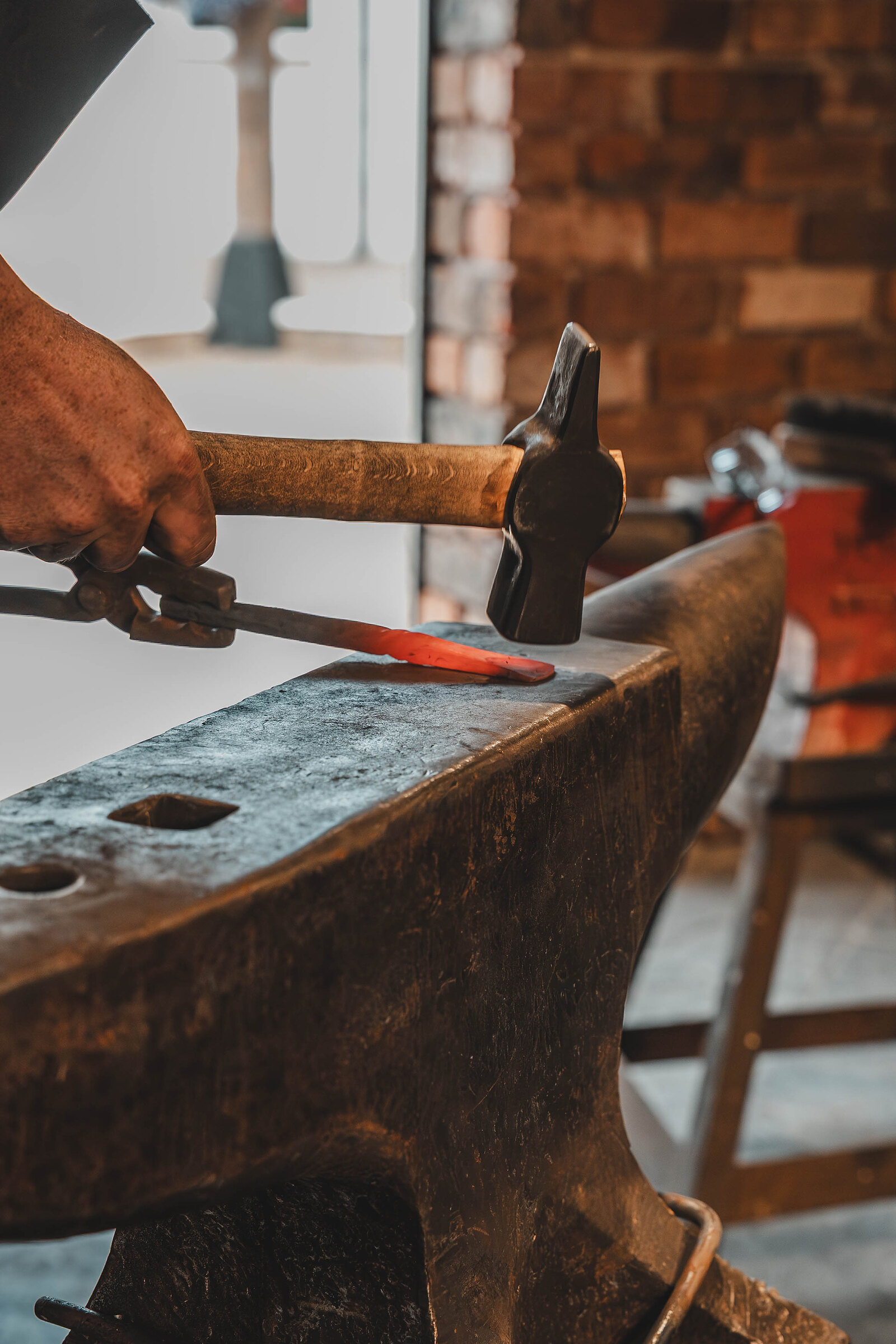 A hammer strikes a glowing bar of steel on the anvil.