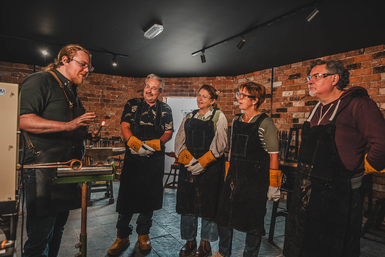 The blacksmith talks a group in aprons and gloves through the session at the Forge.