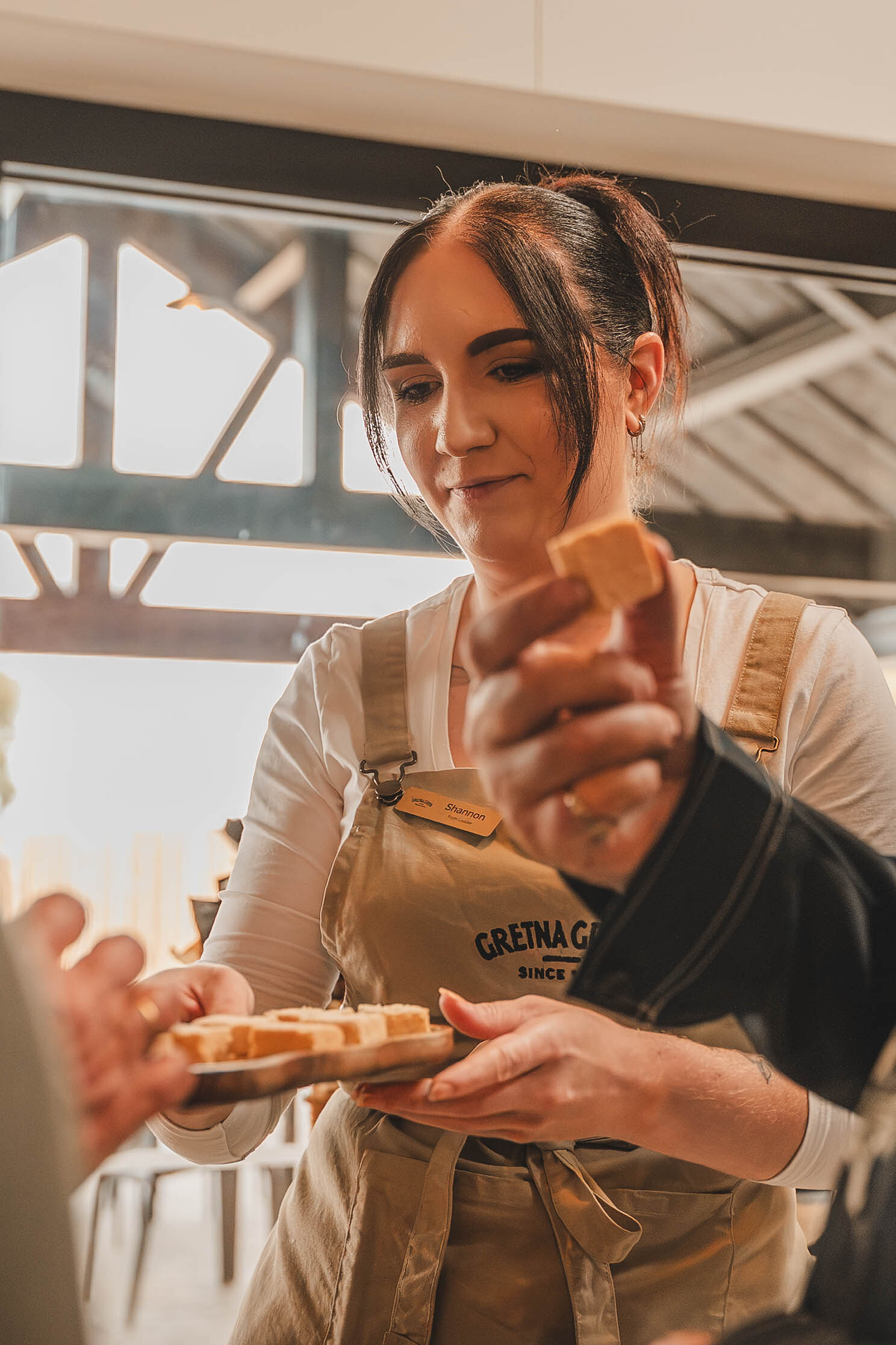 A host in a Gretna Green apron offers a tray of tasting samples.