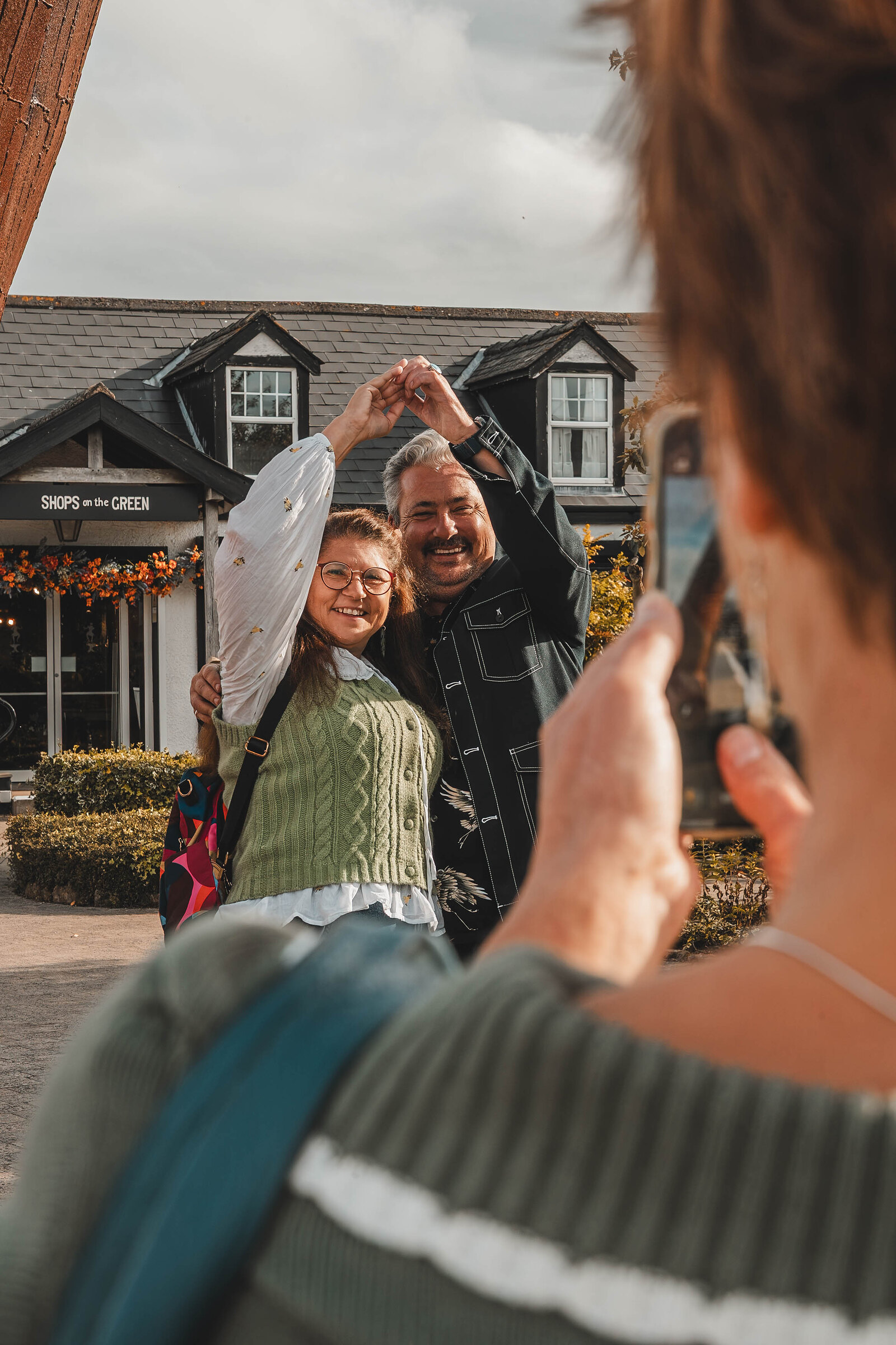 A visitor photographs a couple making a heart with their hands in the courtyard.