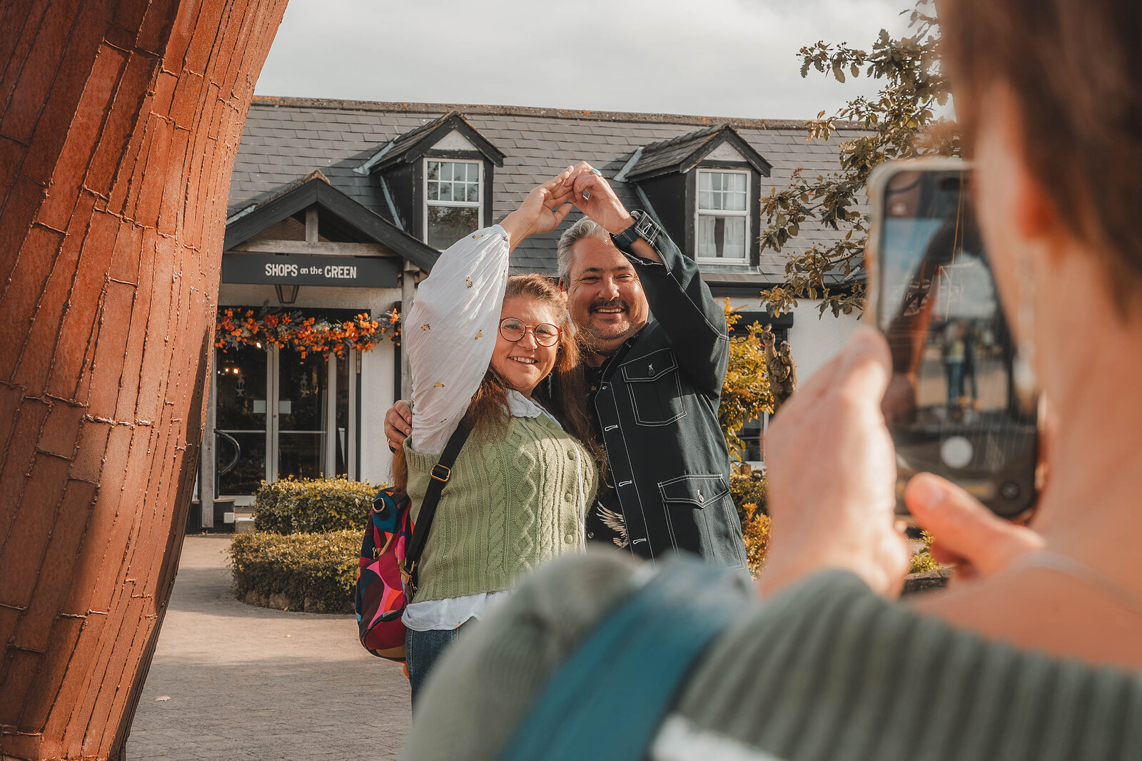 A couple make a heart with their hands for a photograph outside the Shops at the Green.