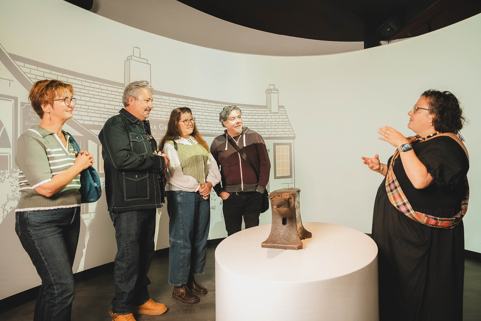 A guide in a tartan sash tells a group the story of the anvil in the Famous Blacksmiths Shop museum.