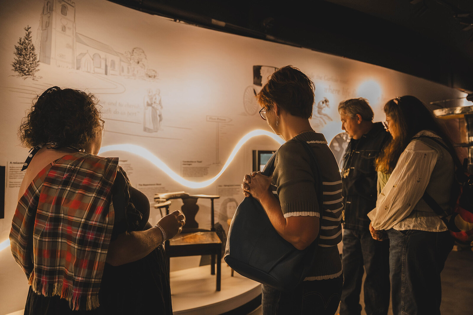 Visitors follow the guide through the museum's exhibition, lit by a ribbon of light along the wall.
