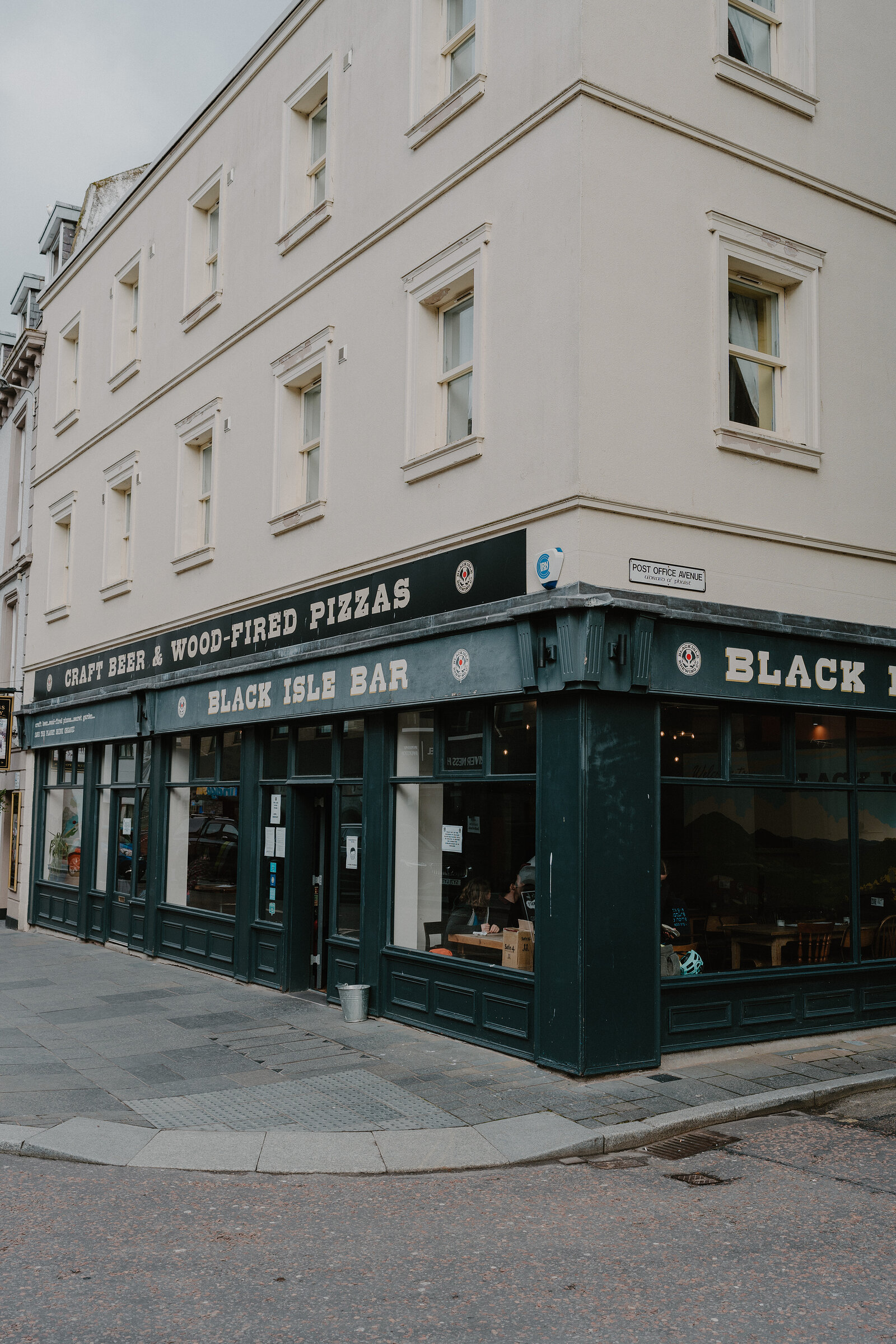 A dark green corner shopfront carries signage reading "CRAFT BEER & WOOD-FIRED PIZZAS" and "BLACK ISLE BAR", large windows looking into the bar beyond.